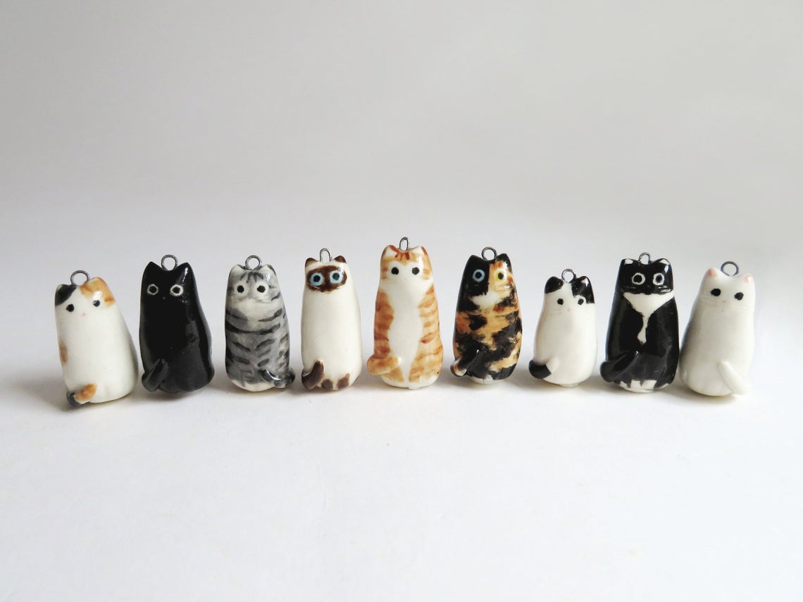 Cute Cat Necklace options from left to right: calico, black, gray tabby, siamese, orange tabby, tortoiseshell, white with black spots, tuxedo, and white