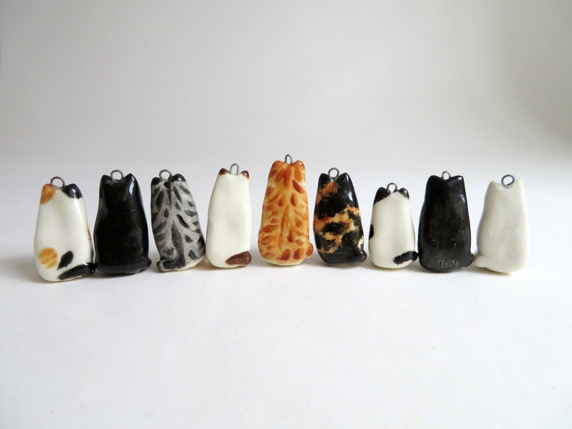 Back side of Cute Cat Necklace charm options from left to right: calico, black, gray tabby, siamese, orange tabby, tortoiseshell, white with black spots, tuxedo, and white