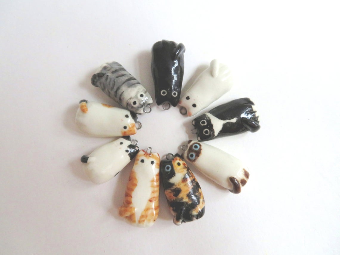 Circle up Cute Cat Necklace options from left to right: calico, black, gray tabby, siamese, orange tabby, tortoiseshell, white with black spots, tuxedo, and white